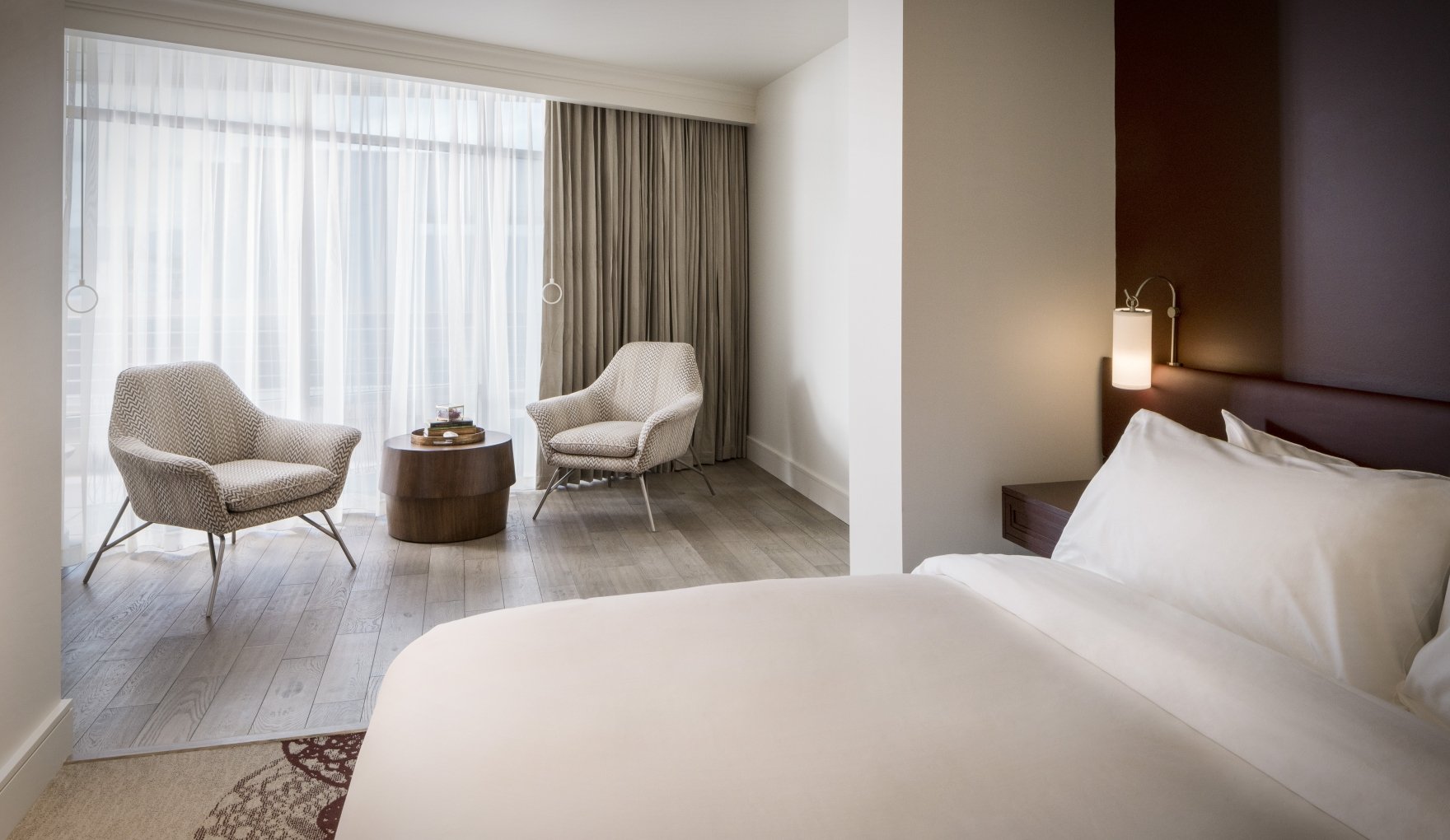 The bedroom of an Executive Suite at the Elizabeth Hotel in Fort Collins, featuring a large bed, seating area and a bright window