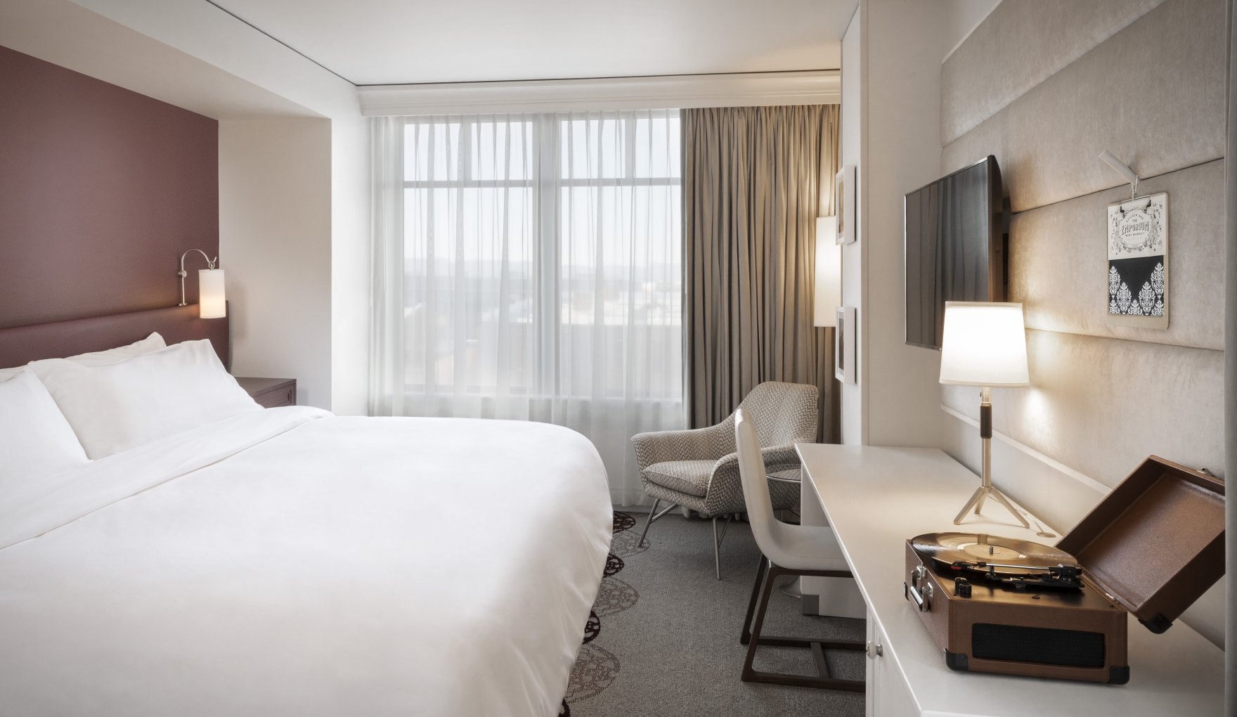 A standard King room at the Elizabeth Hotel in Fort Collins, featuring a large bed, wall-mounted TV and bright window