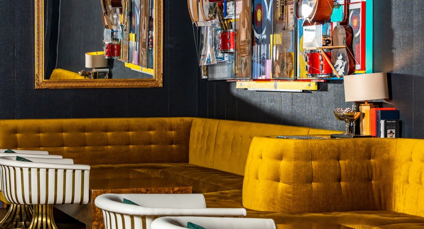 The dining room of the Magic Rat at The Elizabeth hotel, featuring a wall of gold fabric benches and a music-themed wall-mounted collage