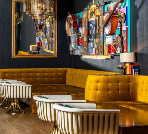 The dining room of the Magic Rat at The Elizabeth hotel, featuring a wall of gold fabric benches and a music-themed wall-mounted collage