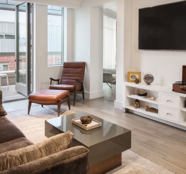 A bright, modern living room with floor-to-ceiling windows, a white sofa, and a leather armchair.