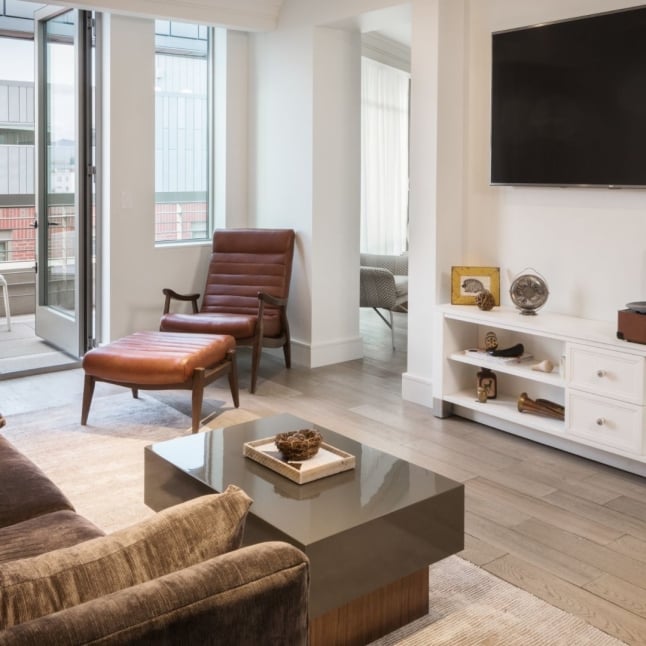 A bright, modern living room with floor-to-ceiling windows, a white sofa, and a leather armchair.