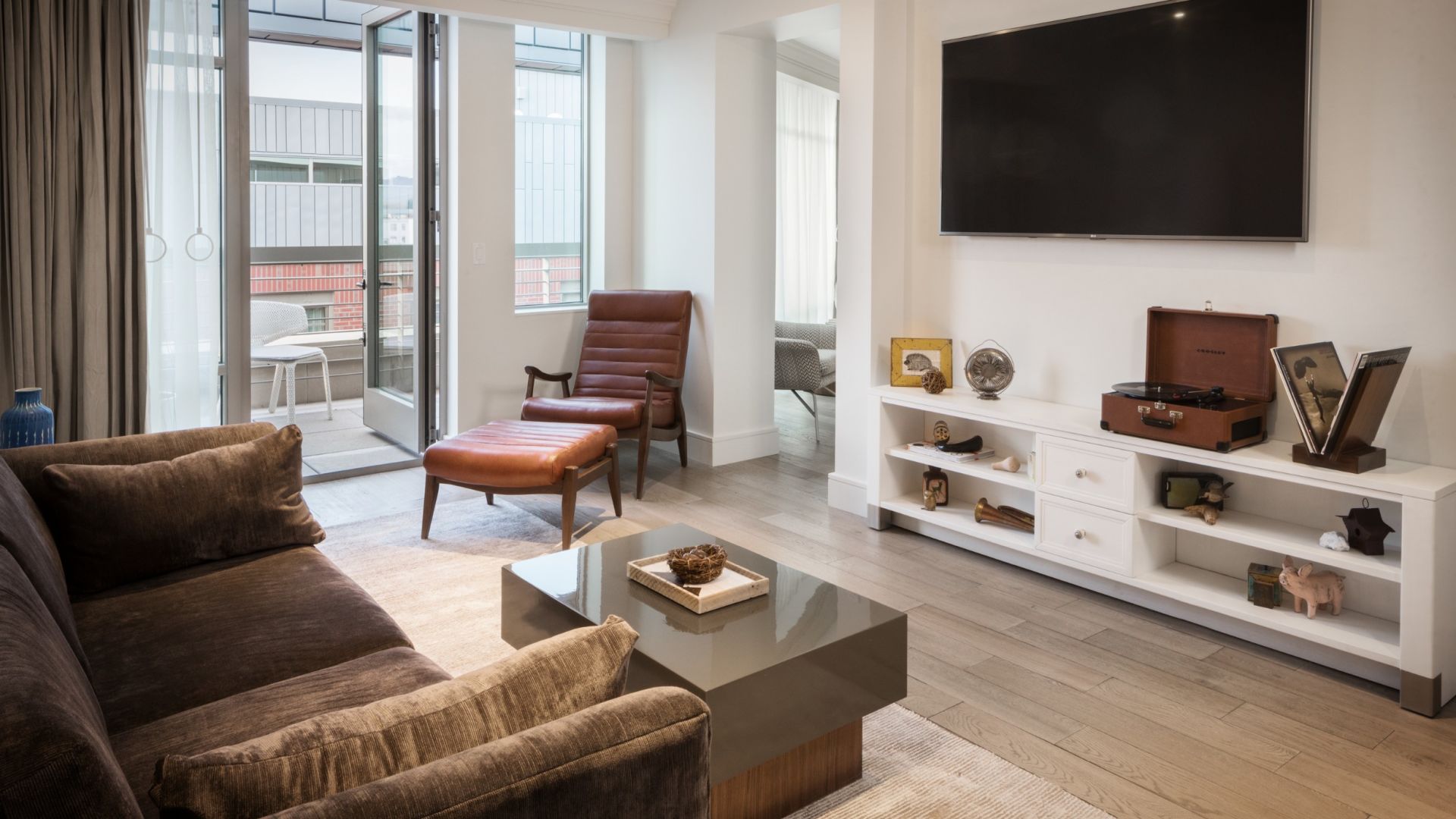 A bright, modern living room with floor-to-ceiling windows, a white sofa, and a leather armchair.
