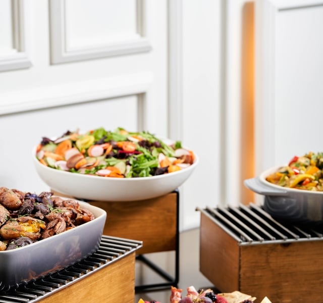 A catering spread featuring a large bowl of fresh green salad and other hot food items in chafing dishes.