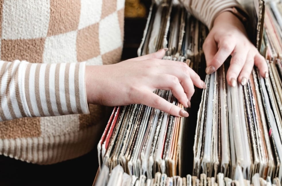 A person's hands Browse through a shelf of vinyl records, with colorful album spines visible.