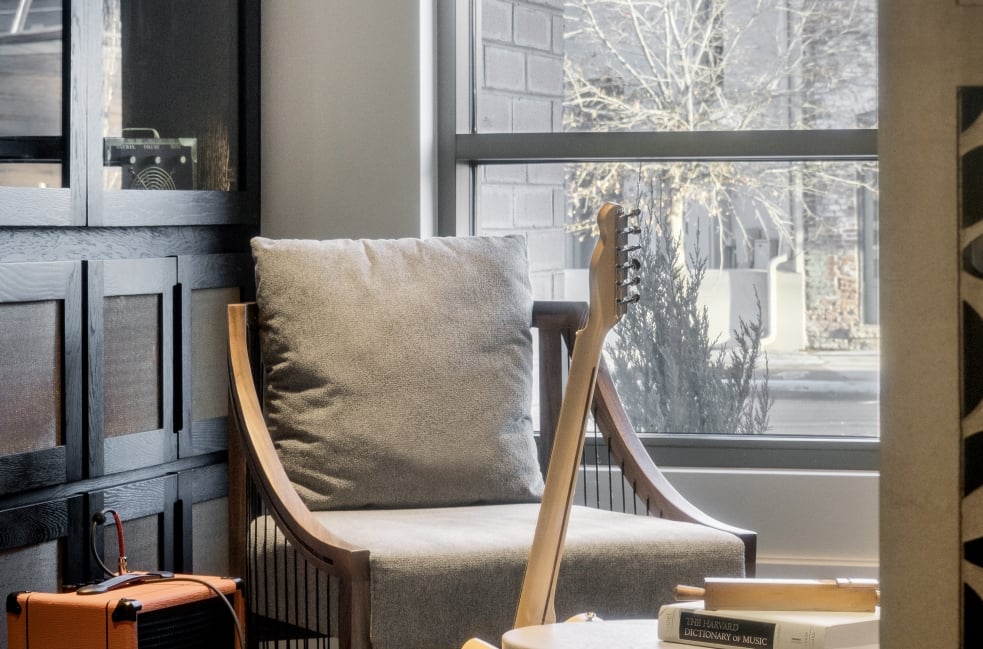 A close-up shot of a modern, grey upholstered armchair with tufted detailing, seen from the side.