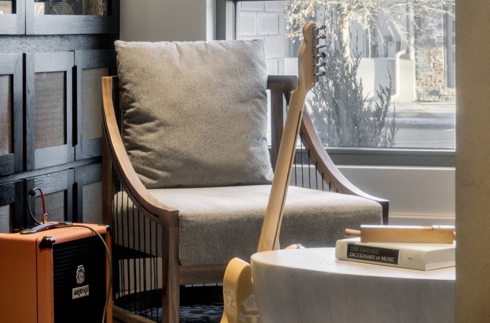 A close-up shot of a modern, grey upholstered armchair with tufted detailing, seen from the side.
