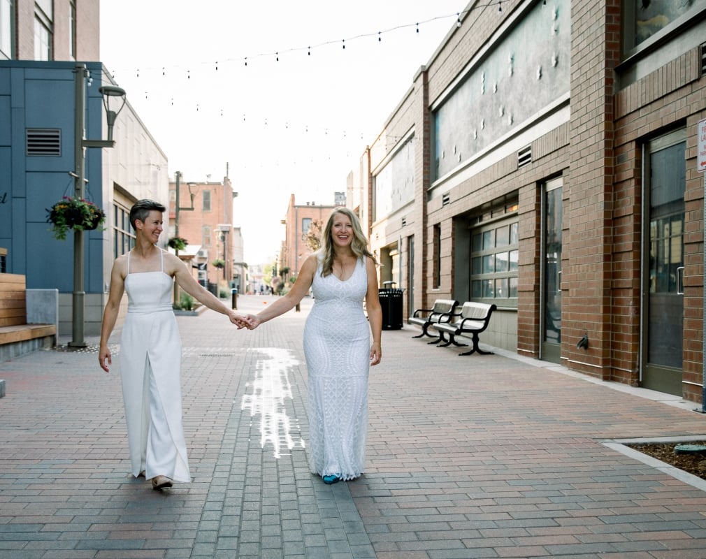 A bride and groom in the distance, walking together down a wide, modern city alley.