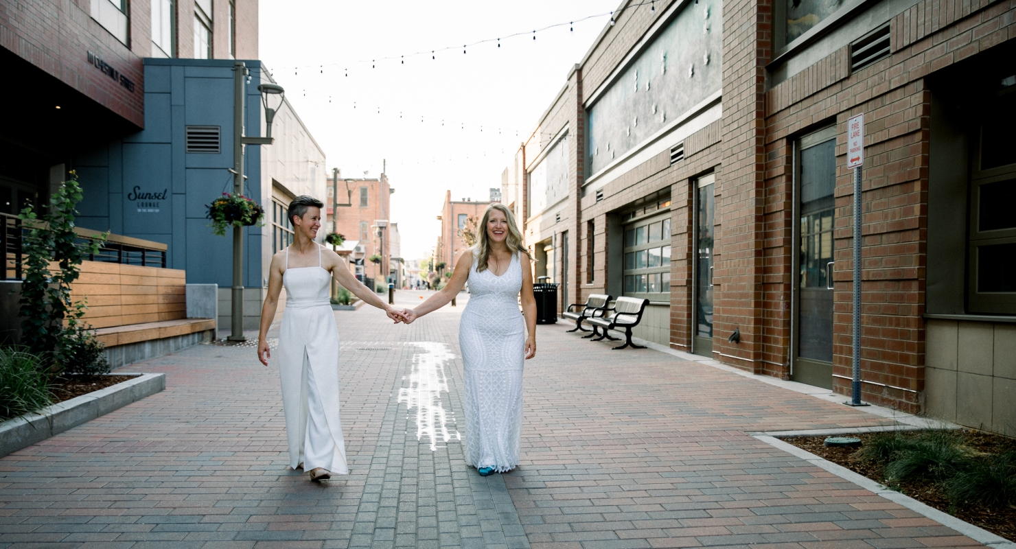 A bride and groom in the distance, walking together down a wide, modern city alley.