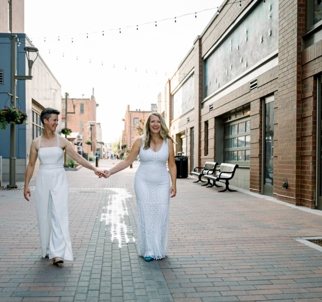 A bride and groom in the distance, walking together down a wide, modern city alley.