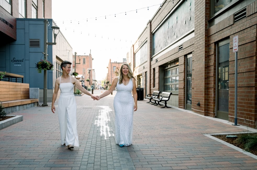 A bride and groom in the distance, walking together down a wide, modern city alley.