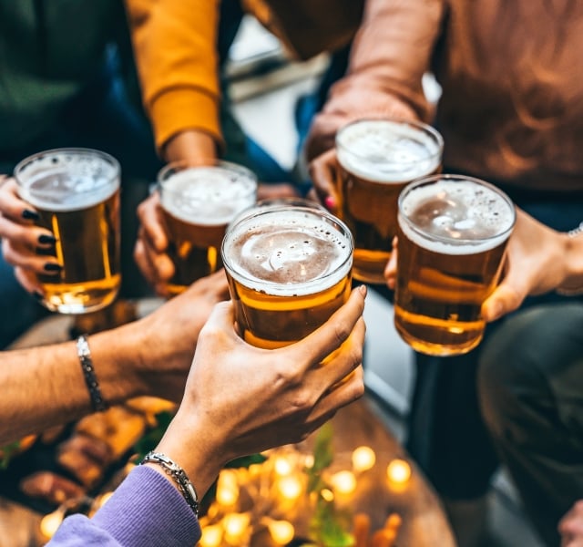 Group of friends drinking and toasting glass of beer at brewery pub restaurant- Happy multiracial people enjoying happy hour with pint sitting at bar table- Youth Food and beverage lifestyle concept