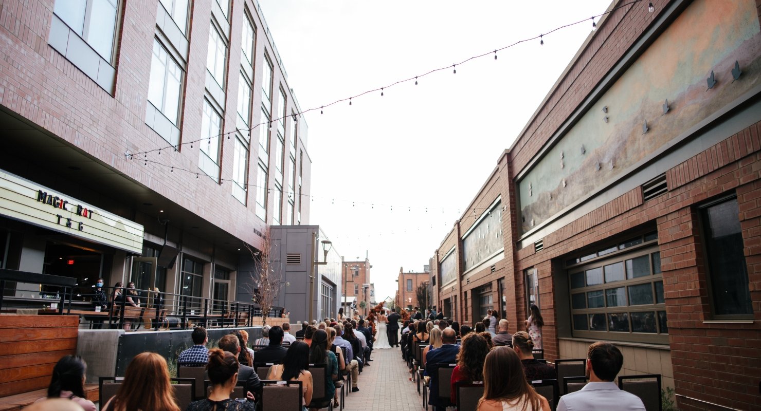 People dining outdoors at night at restaurants lining a brick alleyway, under glowing string lights.