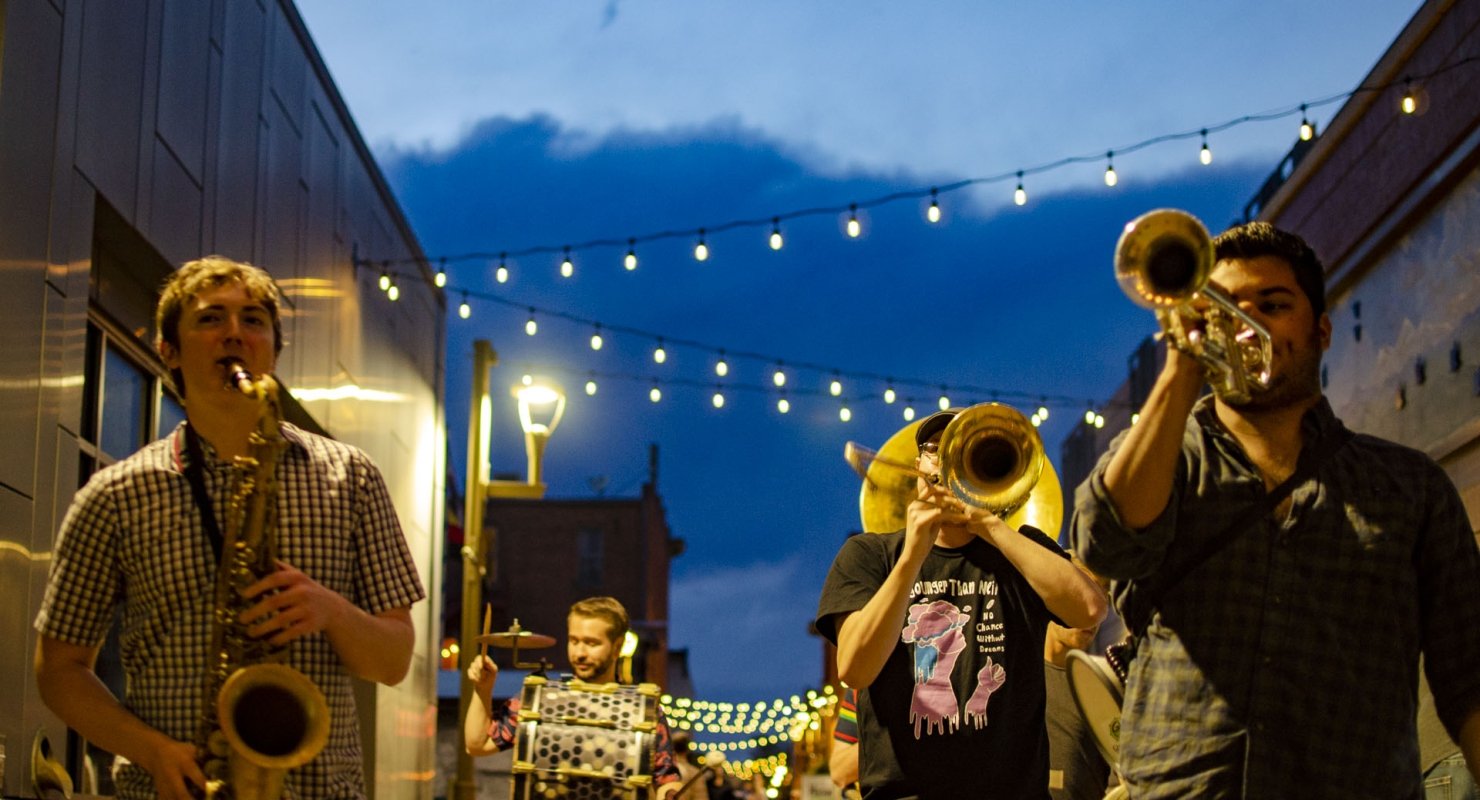 An evening event in a brick alleyway, illuminated by string lights, with a musician playing the saxophone.