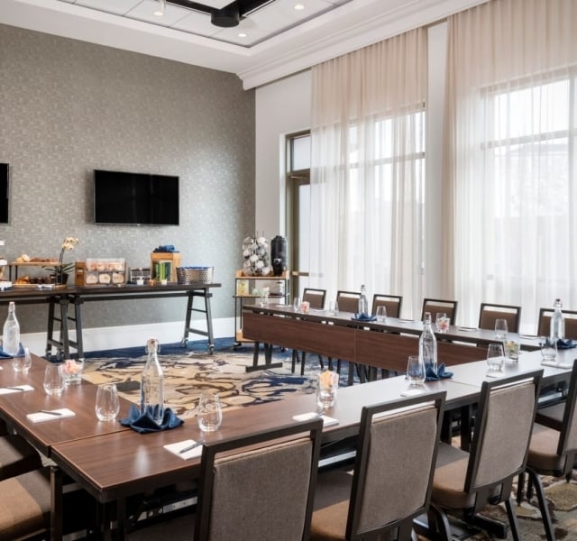 A modern conference or dining room with a long table, black chairs, and contemporary lighting.