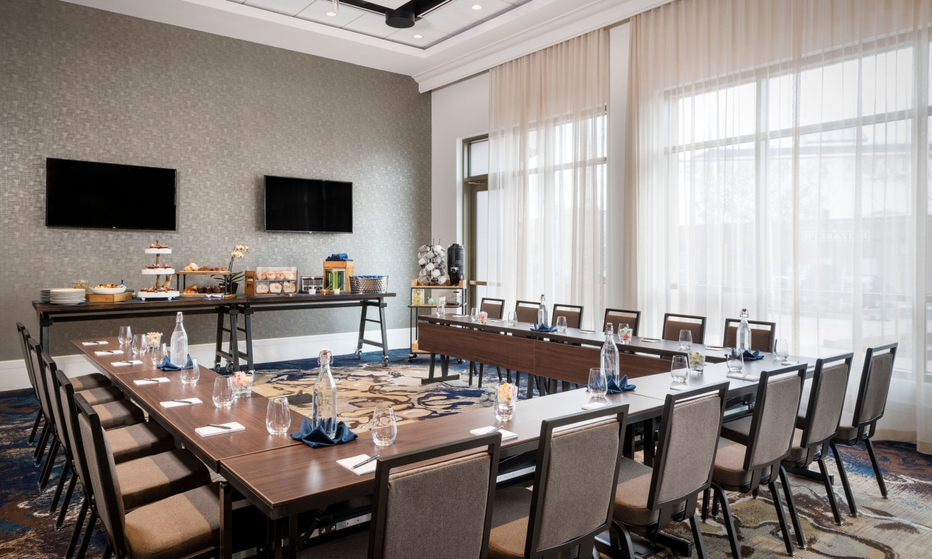 A modern conference or dining room with a long table, black chairs, and contemporary lighting.