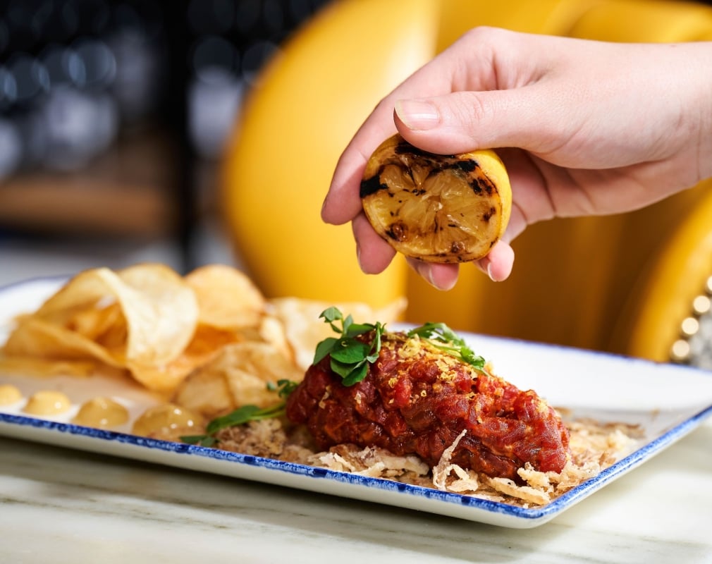 A hand squeezes burnt lemon onto a saucy chicken dish