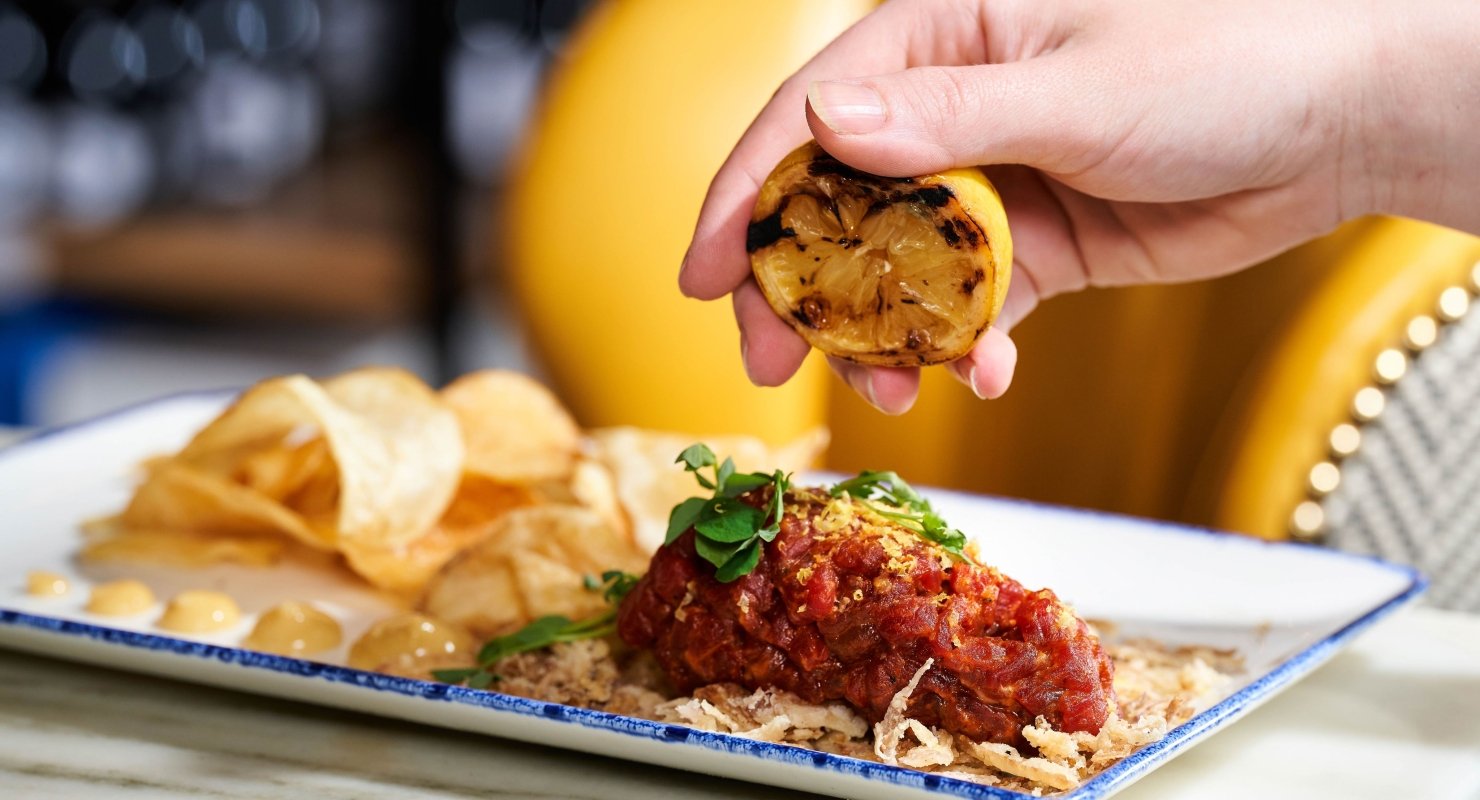 A hand squeezes burnt lemon onto a saucy chicken dish