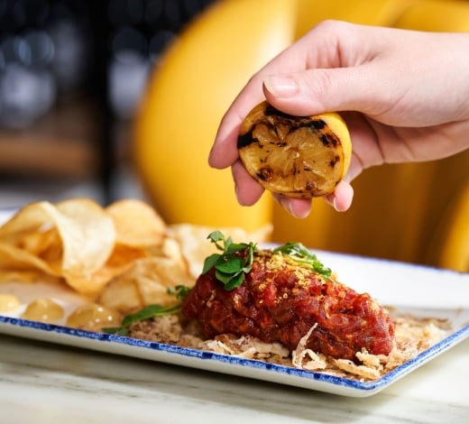 A hand squeezes burnt lemon onto a saucy chicken dish