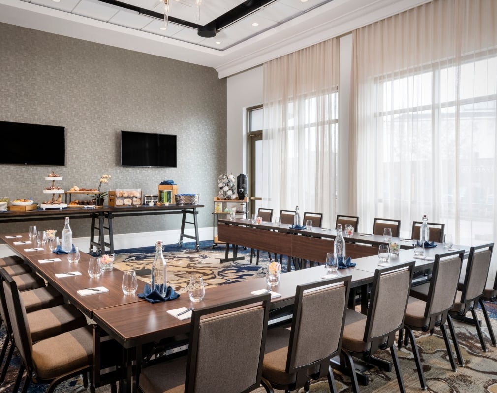 A boardroom at the Elizabeth, with desks and chairs set up in a Hollow square configuration and two wall-mounted TVs