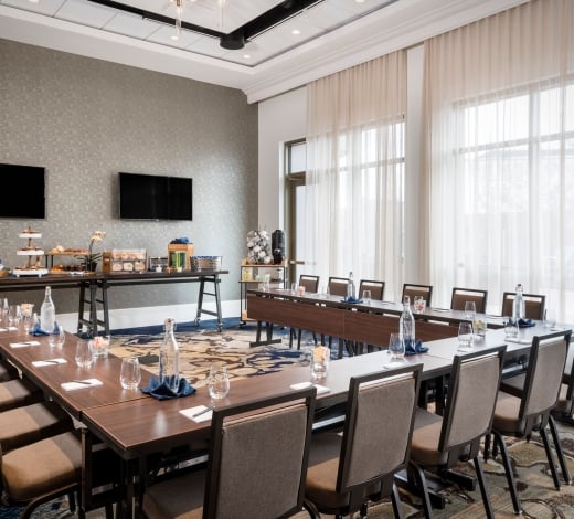 A boardroom at the Elizabeth, with desks and chairs set up in a Hollow square configuration and two wall-mounted TVs