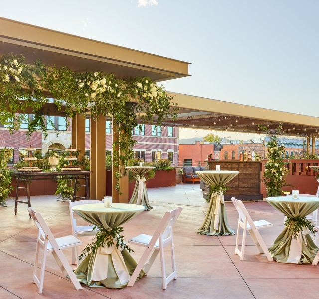 A terrace at the Elizabeth hotel set up for a reception, with several cruiser tables covered in white lines and decorated with flowers