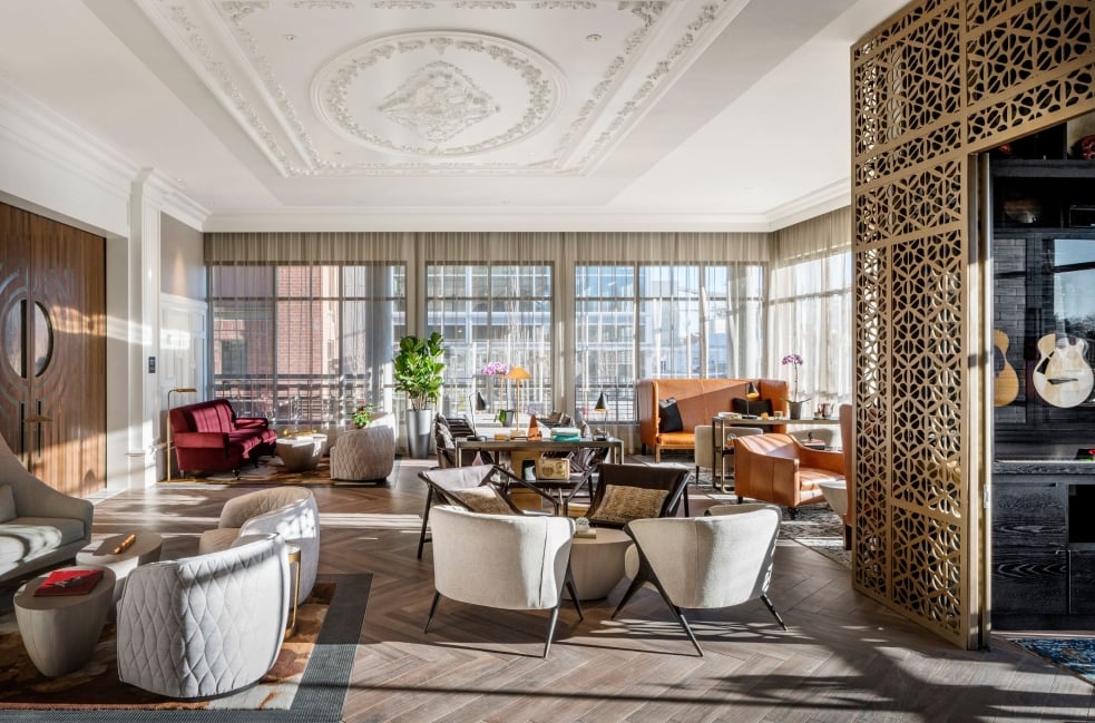 The instrument lending room at the Elizabeth Hotel, a case full of wall-mounted guitars within a gold wrought iron fenced area, next to an adjoining salon with wraparound windows