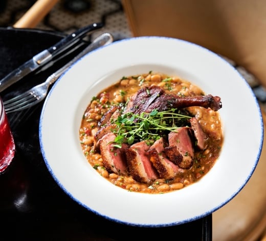 A dish consisting of a duck leg and breast on a bean cassoulet
