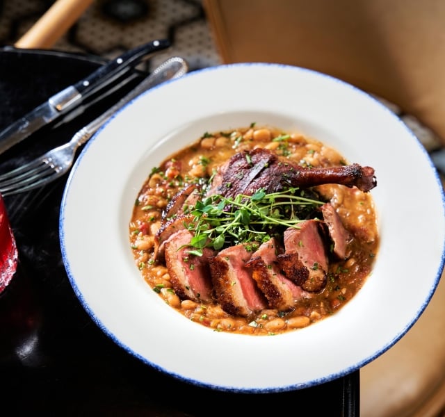 A dish consisting of a duck leg and breast on a bean cassoulet
