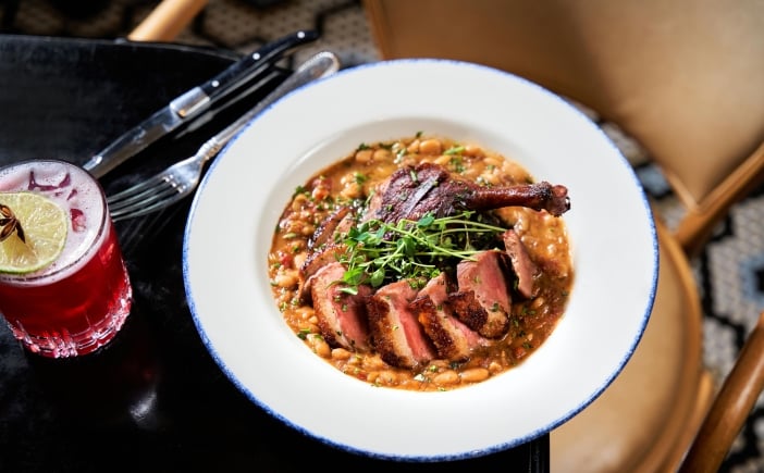 A dish consisting of a duck leg and breast on a bean cassoulet