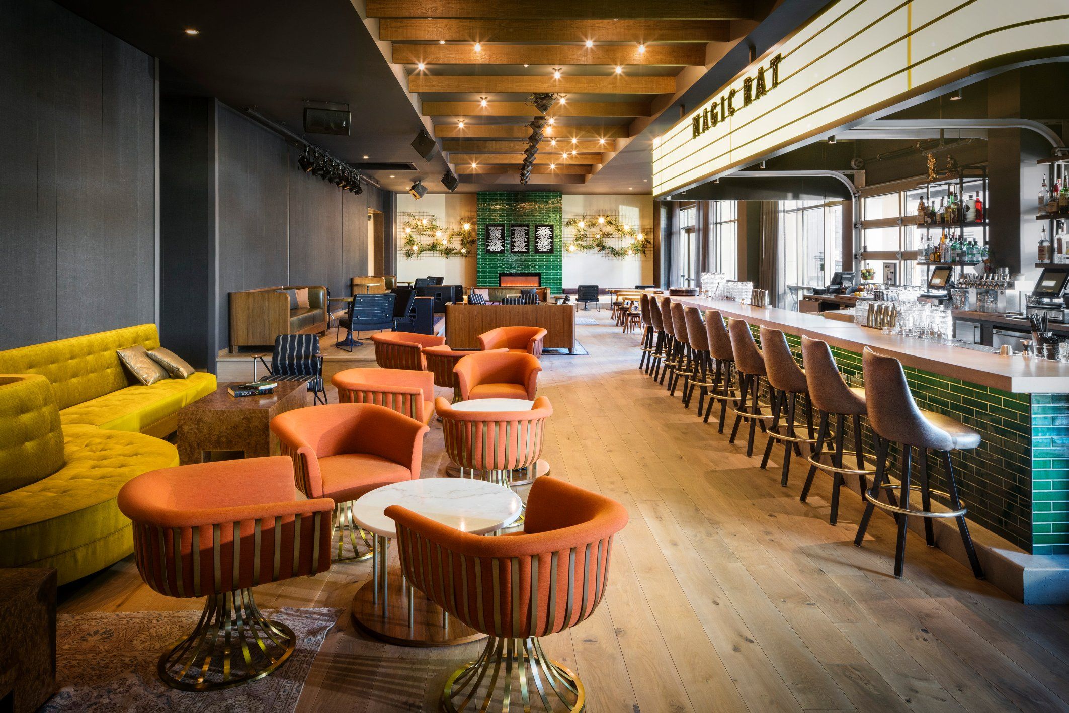 The bar at Magic Rat, a live music venue in the Elizabeth Hotel, featuring warm recessed lighting, a long bar and retro orange chairs around round tables