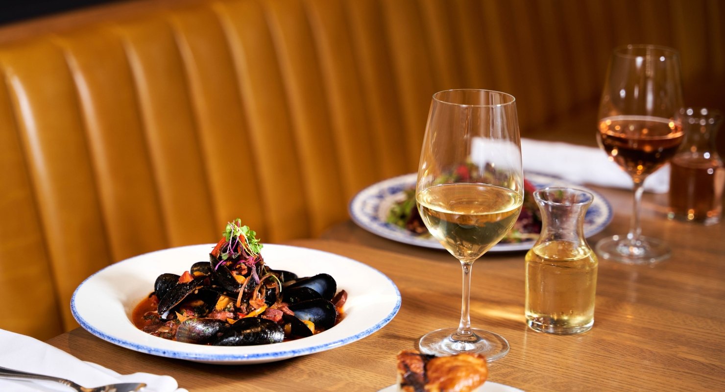 A large bowl of mussels accompanied by glasses of white wine on a restaurant table