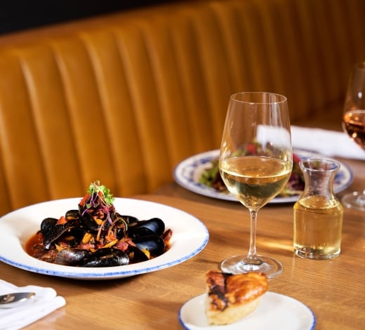 A large bowl of mussels accompanied by glasses of white wine on a restaurant table