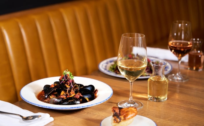 A large bowl of mussels accompanied by glasses of white wine on a restaurant table