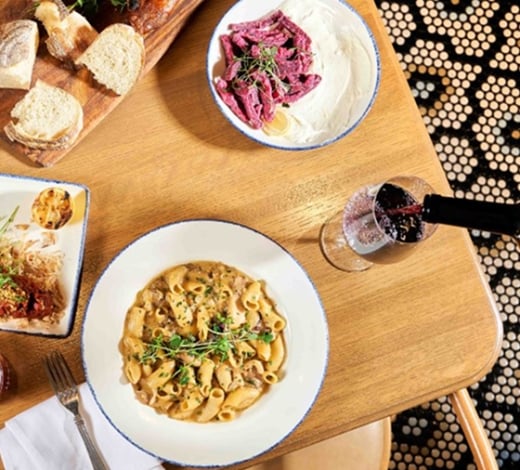 A table full of gourmet dishes, including a white pasta dish, a tray with dips and bread, and a glass of red wine.