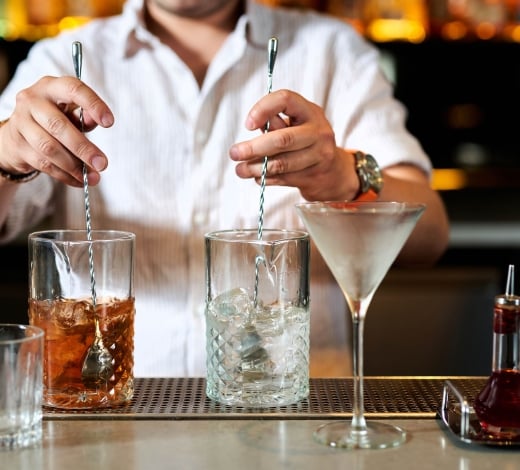 A bartender stirring two cocktails