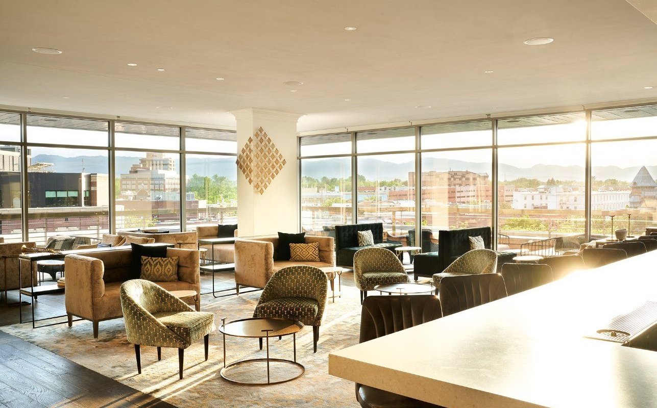 A bright, open seating area at the sunset lounge, with round tables and comfortable chairs and light streaming in from two large bay windows