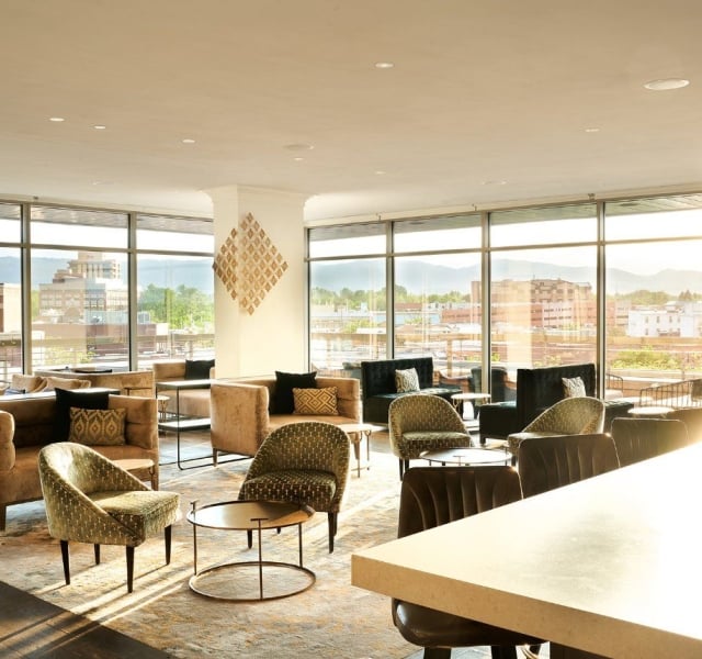 A bright, open seating area at the sunset lounge, with round tables and comfortable chairs and light streaming in from two large bay windows