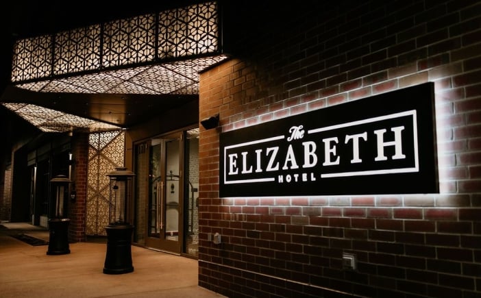 The exterior of the Elizabeth Hotel in Fort Collins, with an illuminated black and white sign on the facade and a marquee-style entryway