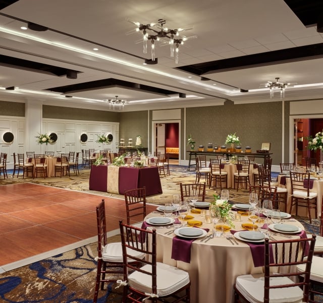 A ballroom set up for a wedding, with flower-topped banquet tables and a dance floor