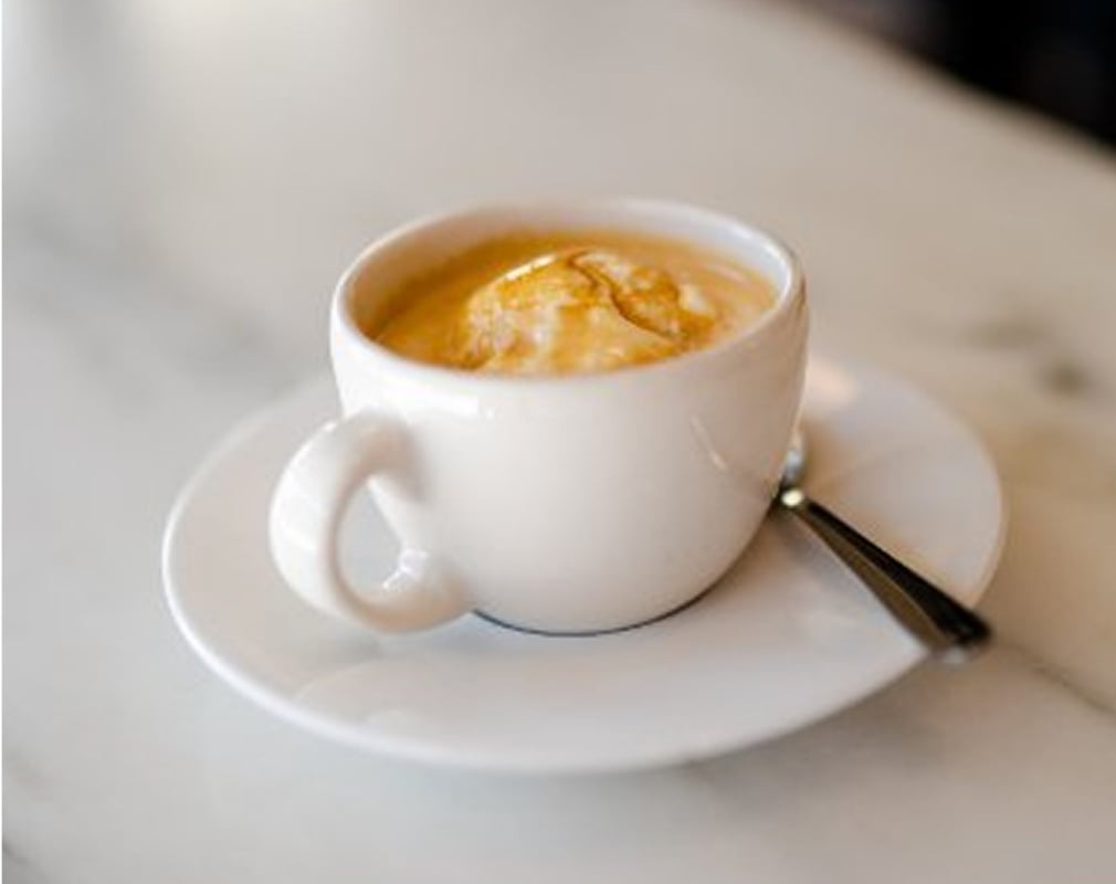 A white coffee cup and saucer on a counter top, with light foam on top and a silver spoon