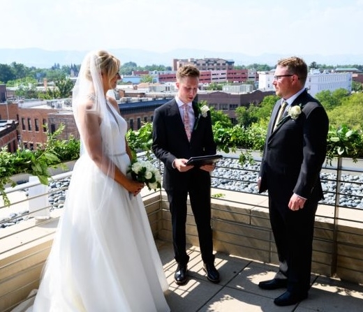 A bride and groom having a wedding ceremony on a balcony of the Elizabeth Hotel, with Fort Collins on the horizon in the background