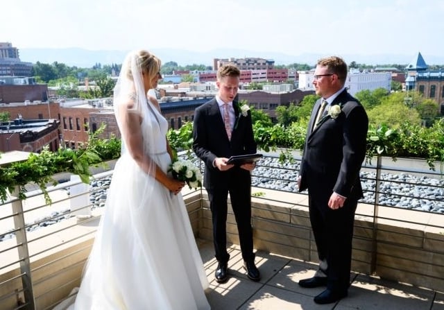 A bride and groom having a wedding ceremony on a balcony of the Elizabeth Hotel, with Fort Collins on the horizon in the background