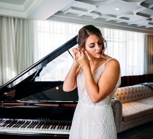 A bride adjust her earring in front of a grand piano as she prepares for her wedding at the Elizabeth Hotel