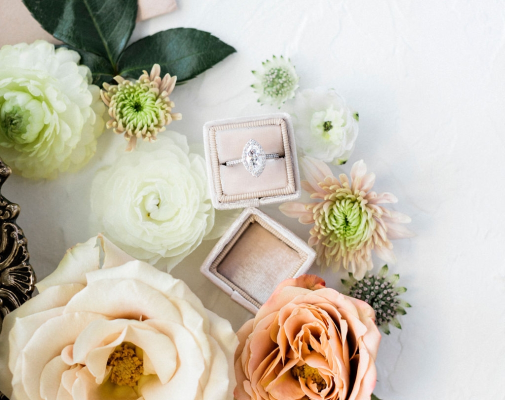 An ornate box with a jewelled engagement ring in it, surrounded by flowers