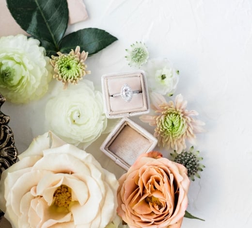 An ornate box with a jewelled engagement ring in it, surrounded by flowers