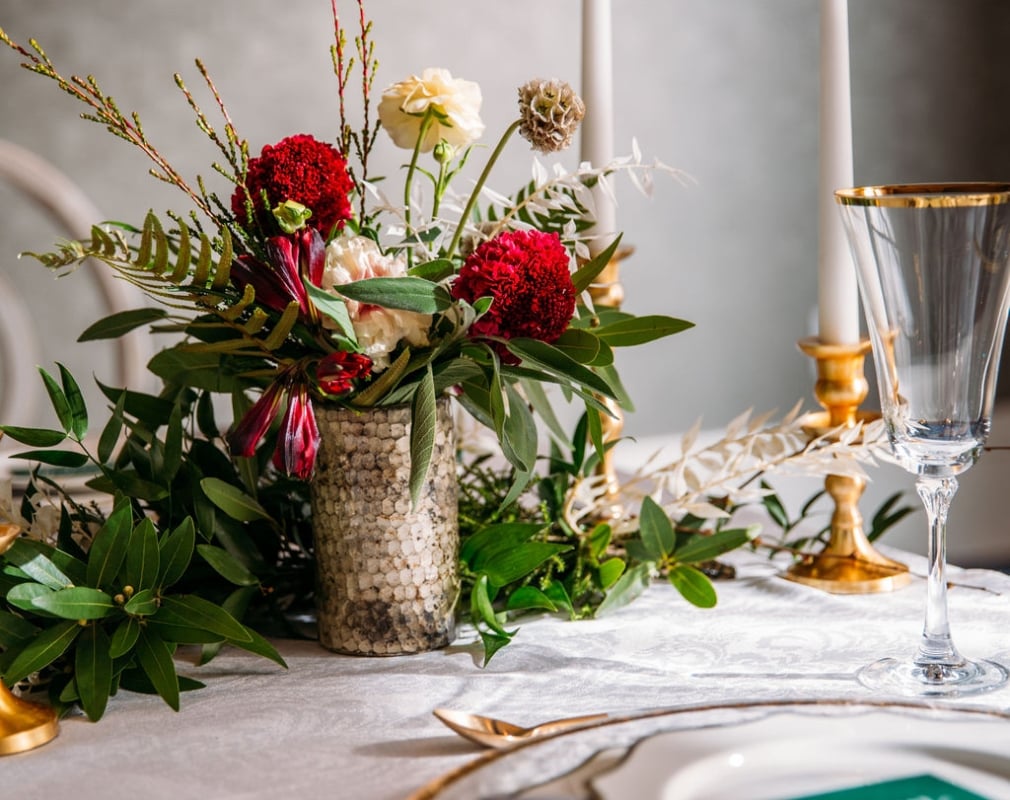 A flowered center piece on a white linen table, accompanied by candlesticks