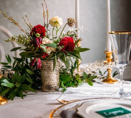 A flowered center piece on a white linen table, accompanied by candlesticks