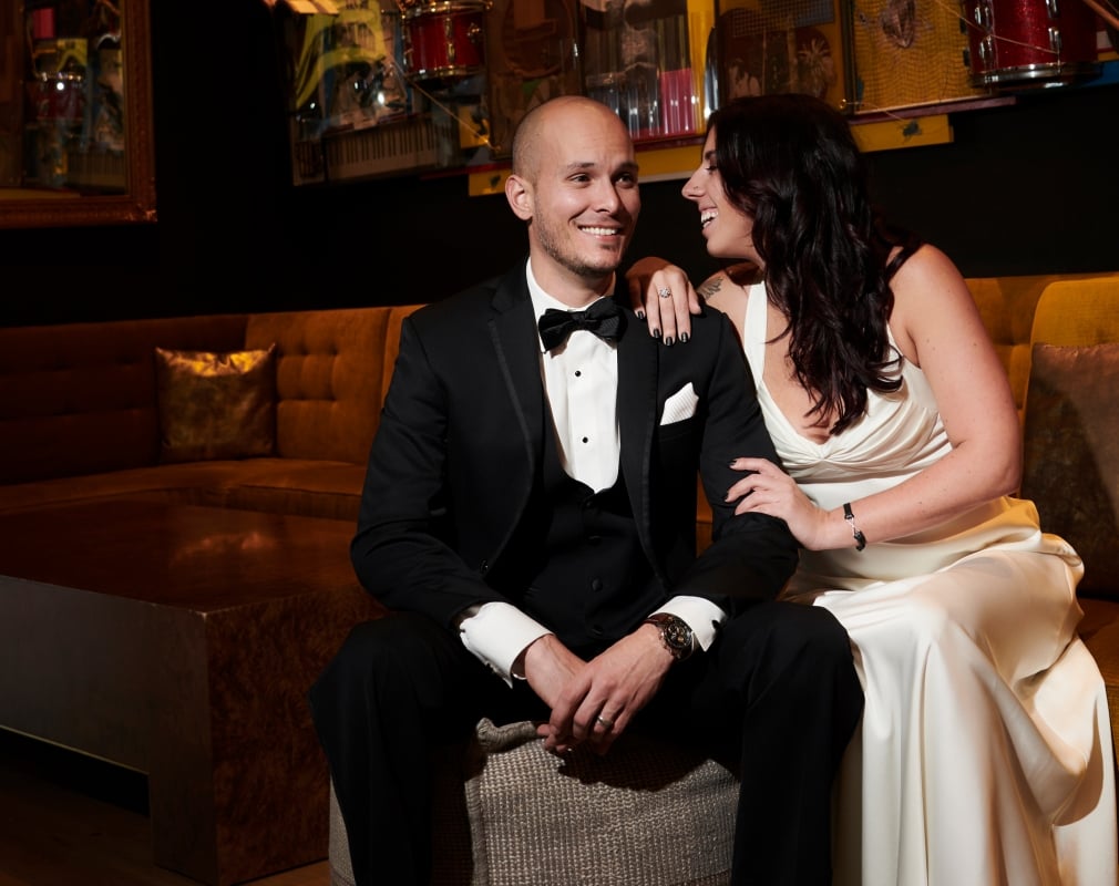 A bride and groom sharing an intimate moment smiling on a gold-fabric couch