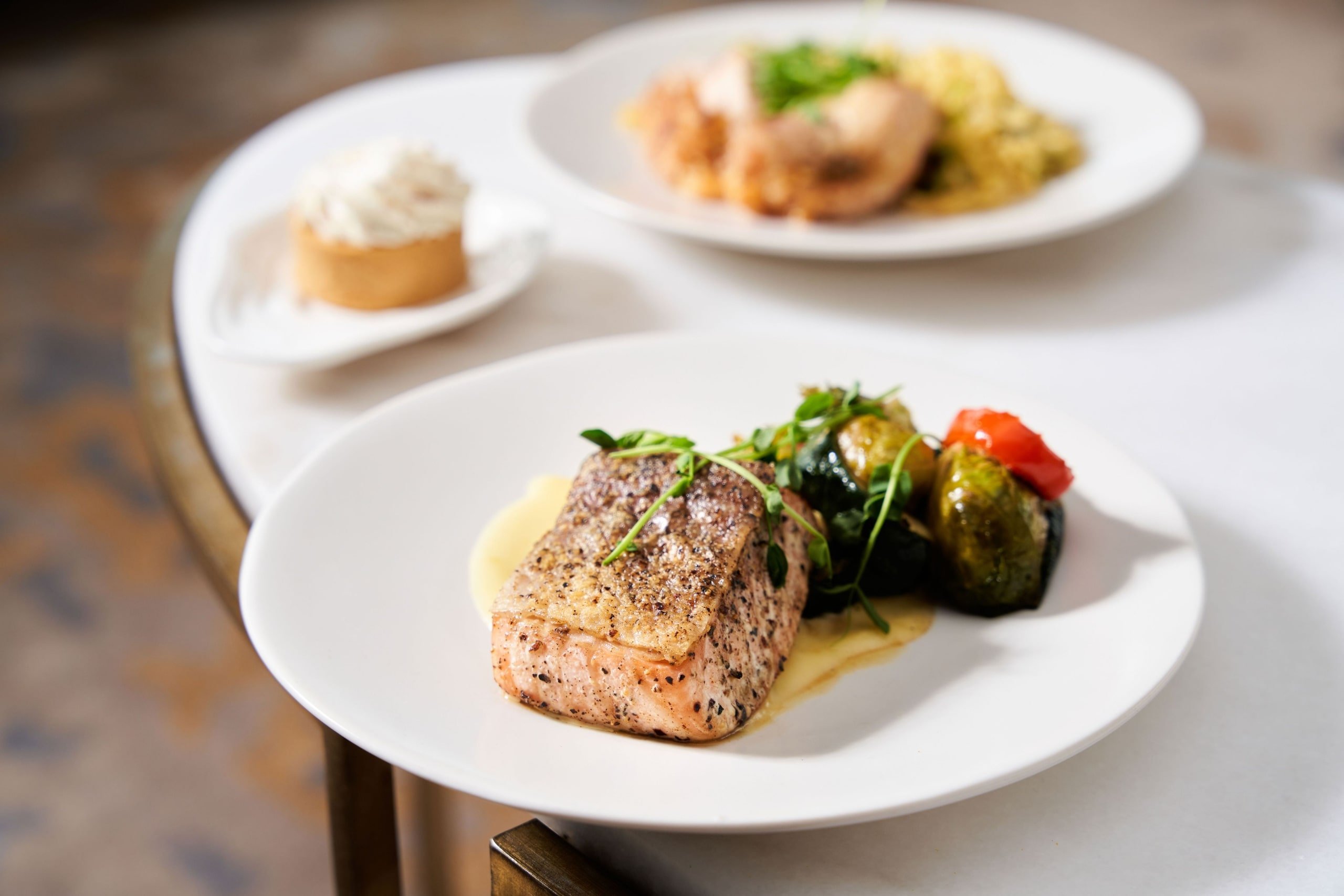 Several elegant dishes on white plates, with a salmon dish with grape leaves in the foreground